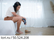 Asian woman with prosthetic leg sitting on bed in the bedroom. Стоковое фото, агентство Ingram Publishing / Фотобанк Лори
