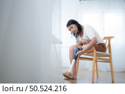 Asian woman with prosthetic leg sitting on chair in the living room. Стоковое фото, агентство Ingram Publishing / Фотобанк Лори