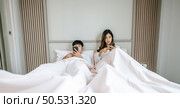 Young Couple lying on bed in bedroom, They are enjoy with social media networks addicts surf the internet on mobile phones ignoring each other, family addicted smartphone concept. Стоковое фото, агентство Ingram Publishing / Фотобанк Лори