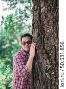 Portrait of Happy Asian man hugging a tree in forest. Protecting and love nature. Environment and ecology concept. Стоковое фото, агентство Ingram Publishing / Фотобанк Лори