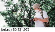 Asian Traveler man wears medical mask with backpack checking a picture on camera at the park with copy space. Travel photographer. Vocation and holiday concept. Стоковое фото, агентство Ingram Publishing / Фотобанк Лори