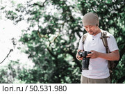 Asian Traveler man with backpack checking a picture on camera at the park with copy space. Travel photographer. Vocation and holiday concept. Стоковое фото, агентство Ingram Publishing / Фотобанк Лори