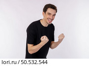 Portrait of happy joyful young man standing doing winner gesture clenching fists keeping isolated on white color wall background studio. Victory and success concept. Стоковое фото, агентство Ingram Publishing / Фотобанк Лори