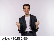 Portrait of happy joyful young businessman standing doing winner gesture clenching fists keeping isolated on white color wall background studio. Victory and success concept. Стоковое фото, агентство Ingram Publishing / Фотобанк Лори