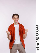 Portrait of happy joyful young man standing doing winner gesture clenching fists keeping isolated on white color wall background studio. Victory and success concept. Стоковое фото, агентство Ingram Publishing / Фотобанк Лори