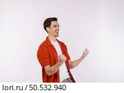 Portrait of happy joyful young man standing doing winner gesture clenching fists keeping isolated on white color wall background studio. Victory and success concept. Стоковое фото, агентство Ingram Publishing / Фотобанк Лори