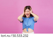 Portrait of angry irritated young woman wearing casual t-shirt covering her ears with hands and shouting while standing isolated over pink background. Expression, people and lifestyle concept. Стоковое фото, агентство Ingram Publishing / Фотобанк Лори