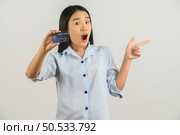 Portrait of positive young asian woman showing credit card good mood salary and pointing finger at aside isolated on white background. Finance, currency, payment and people concept. Стоковое фото, агентство Ingram Publishing / Фотобанк Лори
