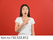 Portrait of Excited young asian woman in white t-shirt pointing finger at aside isolated on red background. Expression and lifestyle concept. Стоковое фото, агентство Ingram Publishing / Фотобанк Лори
