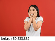 Portrait of Attractive shocked young asian woman in white t-shirt standing isolated on red background. Expression and lifestyle concept. Стоковое фото, агентство Ingram Publishing / Фотобанк Лори