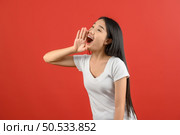 Portrait of Young asian woman in white t-shirt shout story or making announcement isolated on red background. Advertising and lifestyle concept. Стоковое фото, агентство Ingram Publishing / Фотобанк Лори