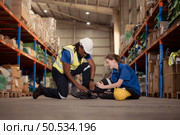 A warehouse worker consoles and helps a female worker who cries out in pain after a leg accident in a large warehouse. Стоковое фото, агентство Ingram Publishing / Фотобанк Лори