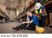 A warehouse worker consoles and helps a female worker who cries out in pain after a leg accident in a large warehouse. Стоковое фото, агентство Ingram Publishing / Фотобанк Лори