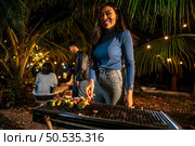 Portrait of Happy Asian young woman cooking meat on barbecue grill at new year party. Bar-B-Q or BBQ on traditional stove. Night Party, people and celebration concept. Стоковое фото, агентство Ingram Publishing / Фотобанк Лори