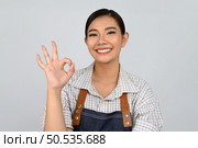 Portrait Asian young woman in waitress uniform and apron showing finger OK sign posture, Pretty woman with body language for feel good isolated on white background, copy space. Стоковое фото, агентство Ingram Publishing / Фотобанк Лори