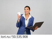 Portrait Asian young woman in officer uniform holding coffee paper cup in hand during working on laptop computer posture,  Pretty girl smiling with happy, isolated on white background. Стоковое фото, агентство Ingram Publishing / Фотобанк Лори