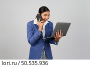 Portrait Asian young woman in officer uniform standing posture talking with mobile phone during working with laptop computer in hand with feel exciting,  isolated on white background. Стоковое фото, агентство Ingram Publishing / Фотобанк Лори