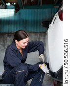 A female mechanic checking the condition of a car’s brake discs and the condition of the tires that have been used for a while. Стоковое фото, агентство Ingram Publishing / Фотобанк Лори