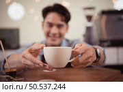 Young barista with the intention of making up a latte coffee to satisfy customers both in appearance and taste, This cup of coffee is ready to be served. Стоковое фото, агентство Ingram Publishing / Фотобанк Лори
