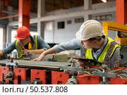 Two young engineers Testing and verifying the operation of the machines forming metal sheet tiles in the factory. Стоковое фото, агентство Ingram Publishing / Фотобанк Лори