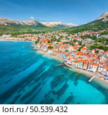 Aerial view of buildings with orange roofs, beach, mountains, blue sea in summer day. Vacation in beautiful Baska city, Krk island, Croatia. Top view of houses, streets, promenade, adriatic sea bay. Стоковое фото, агентство Ingram Publishing / Фотобанк Лори