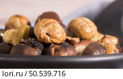 Roasted chestnuts in cast iron pan over rustic wooden board and grey wooden background, selective focus. Стоковое фото, агентство Ingram Publishing / Фотобанк Лори