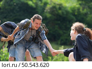 Group of friend on a sunny day in the forest Young group hiker with backpack and trekking poles helping to pull each other up to stand on the log. Стоковое фото, агентство Ingram Publishing / Фотобанк Лори