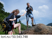 Young woman hiker with backpack and trekking poles with a young man helping to pull him up to stand on the rock. Стоковое фото, агентство Ingram Publishing / Фотобанк Лори