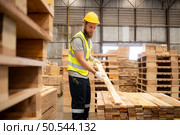 Portrait of young male carpenter working in a woodworking factory, He is wearing a safety helmet and glasses, Checking the wooden planks coming out of the wood grinder. Стоковое фото, агентство Ingram Publishing / Фотобанк Лори