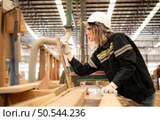 Female carpenter working in a woodworking factory, She is wearing a safety helmet and glasses. Checking the neatness of the planks against the design documents. Стоковое фото, агентство Ingram Publishing / Фотобанк Лори