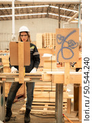 Female carpenter working in a woodworking factory, She is wearing a safety helmet and glasses. Checking the neatness of the planks against the design documents. Стоковое фото, агентство Ingram Publishing / Фотобанк Лори
