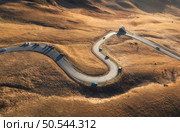 Aerial view of winding road in mountain pass at sunset in golden autumn. Passo Giau, Dolomites, Italy. Beautiful curving roadway, cars, orange grass, alpine meadows. Landscape with highway in fall. Стоковое фото, агентство Ingram Publishing / Фотобанк Лори