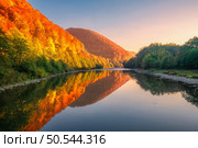 Lake in mountains with red and orange trees at sunset in autumn. Reflection in water. River in carpathian mountains in fall in Ukraine. Landscape with hills with forest in the evening. Amazing nature. Стоковое фото, агентство Ingram Publishing / Фотобанк Лори