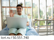 Happy young man using laptop computer while sitting on bed in hospital ward. Стоковое фото, агентство Ingram Publishing / Фотобанк Лори