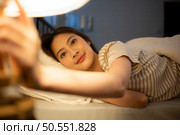 Asian woman lying on the bed turning off the light at the bedside to sleep tonight. Стоковое фото, агентство Ingram Publishing / Фотобанк Лори