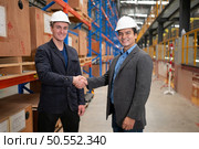 Two businessmen shaking hands in a warehouse It is a warehouse of spare parts and equipment for repairing machinery and passenger cars in the skytrain transportation system. Стоковое фото, агентство Ingram Publishing / Фотобанк Лори