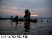 Silhouette of fisherman at sunrise, Standing aboard a rowing boat and casting a net to catch fish for food. Стоковое фото, агентство Ingram Publishing / Фотобанк Лори