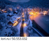 Aerial view of fairy town in snow, road, forest, Jasna lake and houses with lights at night in winter. Top view of mountain village, illumination, snowy pine trees at dusk in Kranjska Gora, Slovenia. Стоковое фото, агентство Ingram Publishing / Фотобанк Лори