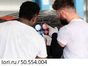Car mechanic working in an auto repair shop, inspecting the operation of the car’s air conditioner and refrigerant. Стоковое фото, агентство Ingram Publishing / Фотобанк Лори