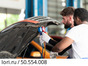 Car mechanic working in an auto repair shop, inspecting the operation of the car’s air conditioner and refrigerant. Стоковое фото, агентство Ingram Publishing / Фотобанк Лори