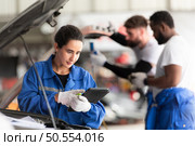 Car mechanic working in an auto repair shop, inspecting the operation of the car’s air conditioner and refrigerant, Focus on woman. Стоковое фото, агентство Ingram Publishing / Фотобанк Лори