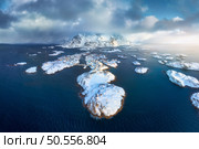 Aerial view of snowy Henningsvaer fishing village, Lofoten islands, Norway in winter at sunset. Top drone view of mountains in snow, sea, boats, cloudy sky, town, rorbuer and houses. Panorama. Scenery. Стоковое фото, агентство Ingram Publishing / Фотобанк Лори