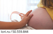 Beautiful pregnant woman sitting near window at home and holding her belly and husband touching unborn child. Стоковое фото, агентство Ingram Publishing / Фотобанк Лори