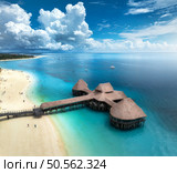 Aerial view of bungalow, white sandy beach, ocean on summer sunny day. Restaurant on the sea. Top drone view of wooden hotel, azure water, palms, sky with slouds. Luxury resort in Kendwa, Zanzibar. Стоковое фото, агентство Ingram Publishing / Фотобанк Лори