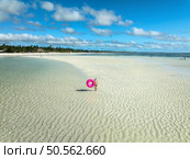 Aerial view of sporty slim woman with swimming ring, sandy beach, blue sea during low tide at sunny summer day in Zanzibar island. Top view of beautiful girl, sandbank, ocean, sky with clouds, palms. Стоковое фото, агентство Ingram Publishing / Фотобанк Лори