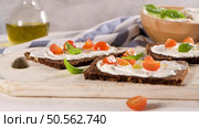 Rye bread bruschetta with cream cheese, olive oil and basil dip, cherry tomatoes, fresh basil leaves on wooden board. Стоковое фото, агентство Ingram Publishing / Фотобанк Лори