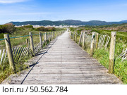 A wooden boardwalk through sand dunes leads to a coastal town of Vila Praia de Ancora nestled against hills. Стоковое фото, агентство Ingram Publishing / Фотобанк Лори