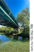 A peaceful river flows beneath a green metal bridge over Rio Ancora iin Portugal, reflecting the blue sky and lush vegetation. Стоковое фото, агентство Ingram Publishing / Фотобанк Лори