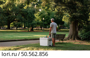 Man standing by a cooler in a park during the late afternoon, enjoying nature and the peaceful surroundings with greenery. Стоковое AI-изображение, AI-художник Сергей Толмачёв / Фотобанк Лори