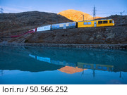 Bernina express train passing by Bianco lake with colorful reflections of the train and mountains during sunset in the swiss alps in autumn. Fall in Switzerland. Yellow modern train with red wagons. Стоковое фото, агентство Ingram Publishing / Фотобанк Лори